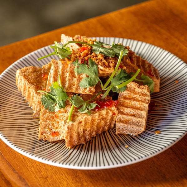 Crispy fried tofu topped with minced pork, chili sauce, and fresh cilantro on a striped plate.