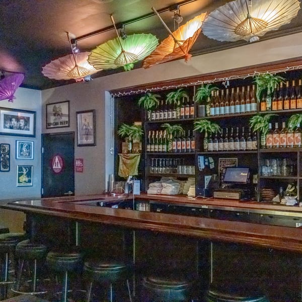 A dimly lit bar at Same Same Thai, with colorful umbrellas on the ceiling and bottles on shelves.
