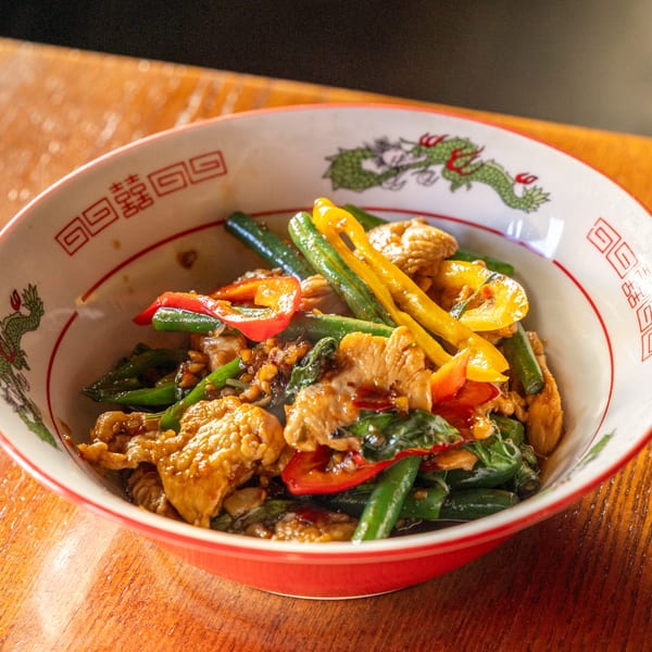 Same Same Thai's Pad Krapow with chicken, green beans, and bell peppers in a dragon-patterned bowl.