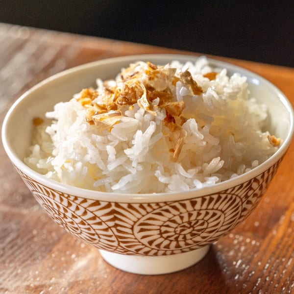 A bowl of white rice topped with crispy fried garlic, served in a patterned bowl.