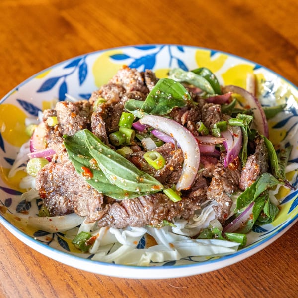 Same Same Thai's beef salad with red onions, green onions, and basil on a patterned plate.